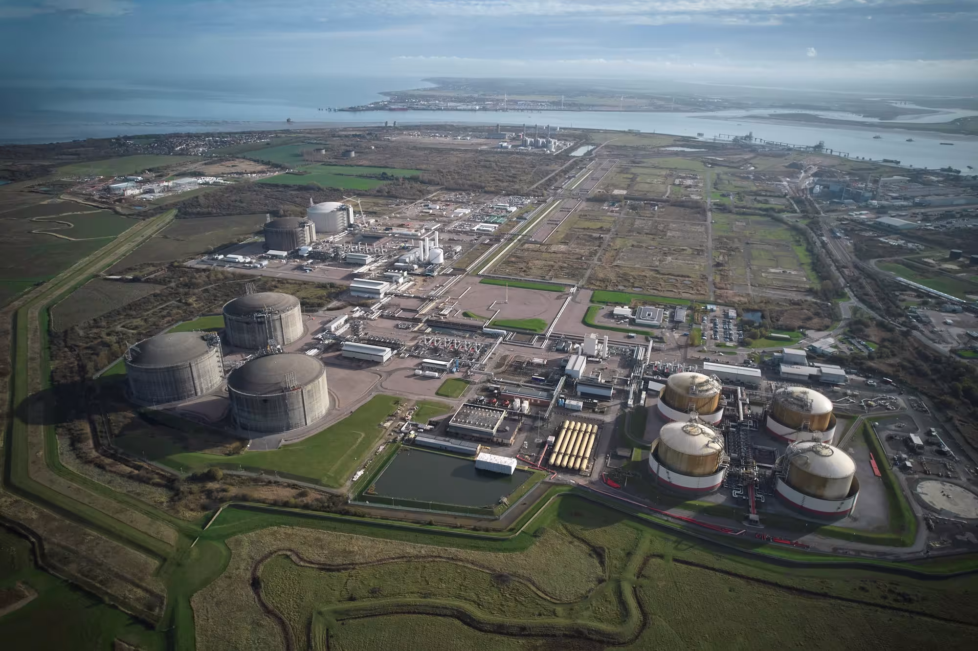 Aerial view of an industrial facility with large white storage tanks surrounded by green fields